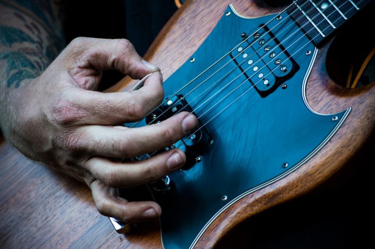 Person plucking guitar with a guitar pick