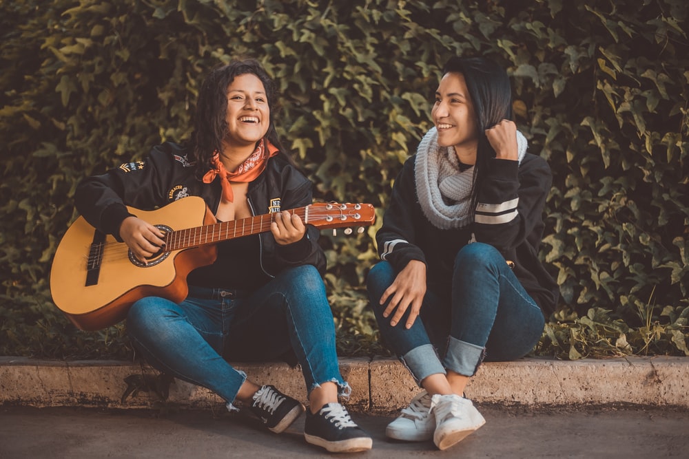 A woman playing the guitar sitting beside a girl wearing a scarf