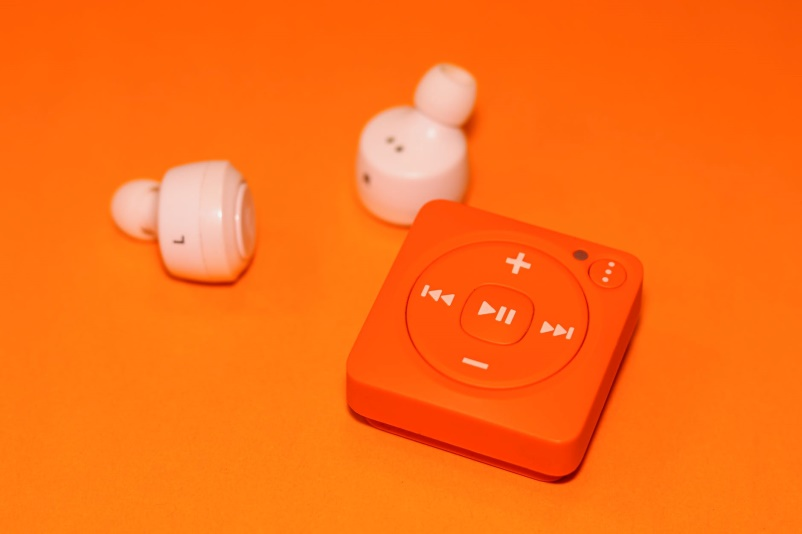 An orange music player along with wireless earphones