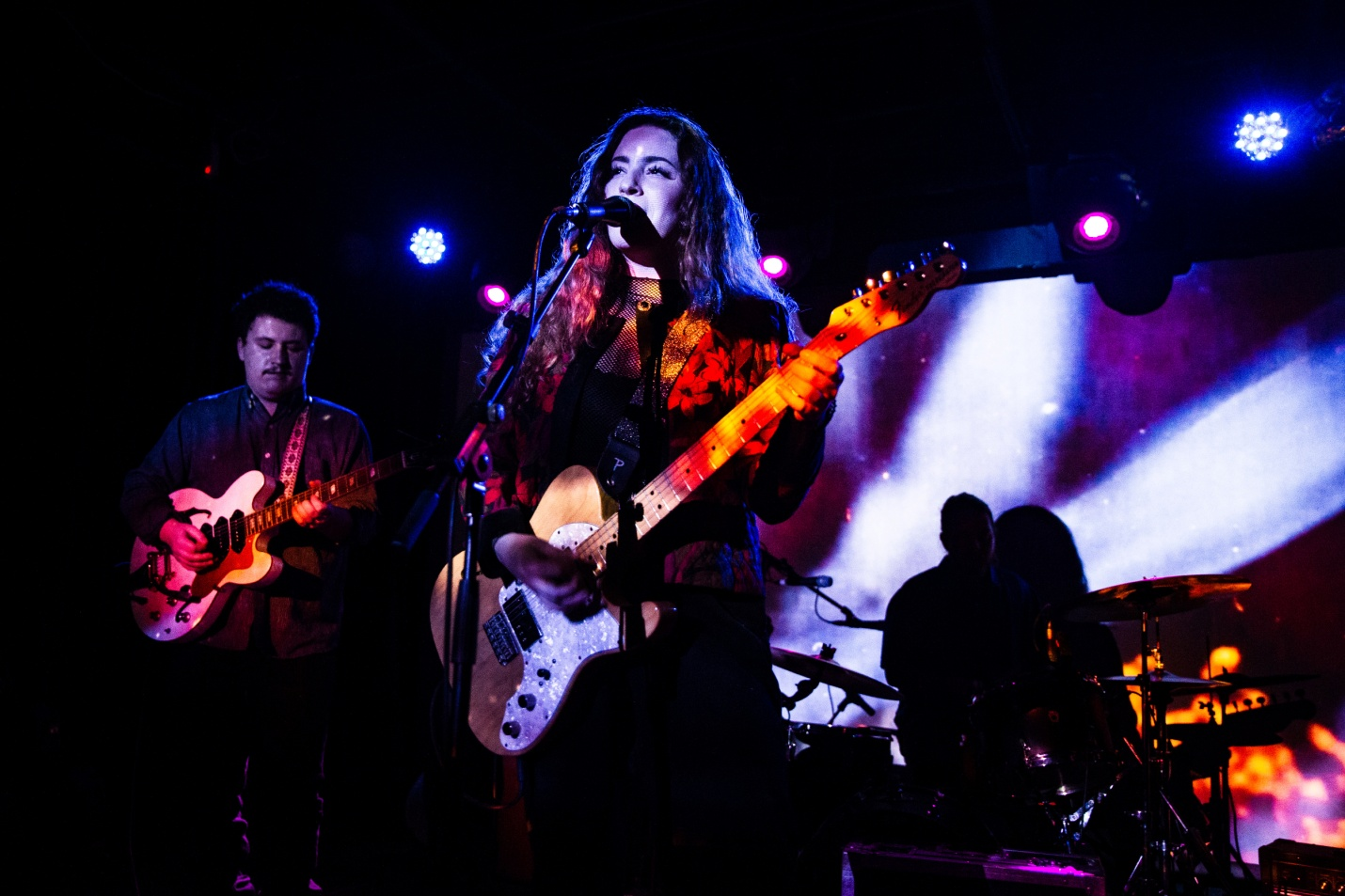 A band playing on stage led by a woman singing and playing the guitar